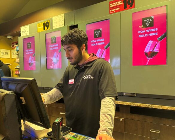 Simerdeep DHaliwal behind a cash register at a gas station, looking at and pushing something on the screen.